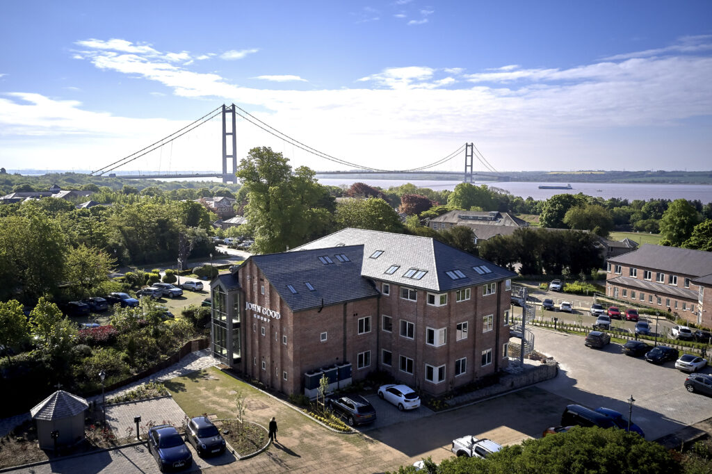 Image taken from a height, overlooking Hesslewood Office Park. Showing a 3 story office, parkland and trees, and the Humber Bridge in the background