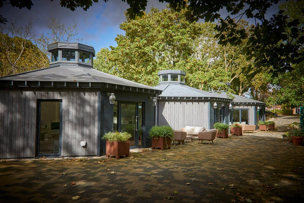 Side view of 3 wooden clad hexagonal shaped, single story buildings
