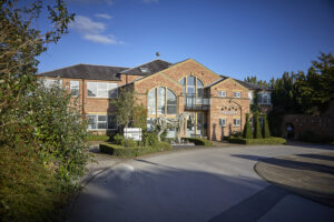 view across a road of a 2 storey brick-built office building, Signage for Cranswick Plc on the building, and a wooden horse sculpture to the front of the building