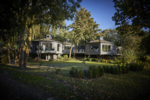 Grey wooden 'treetop' style building. 3 'pod' fronts showing glass balconies. surrounded by tress and grassland