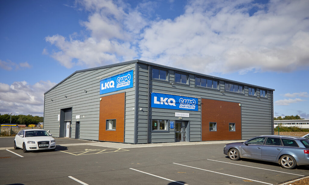 view from across a car park, of a grey steel and wood clad light industrial unit