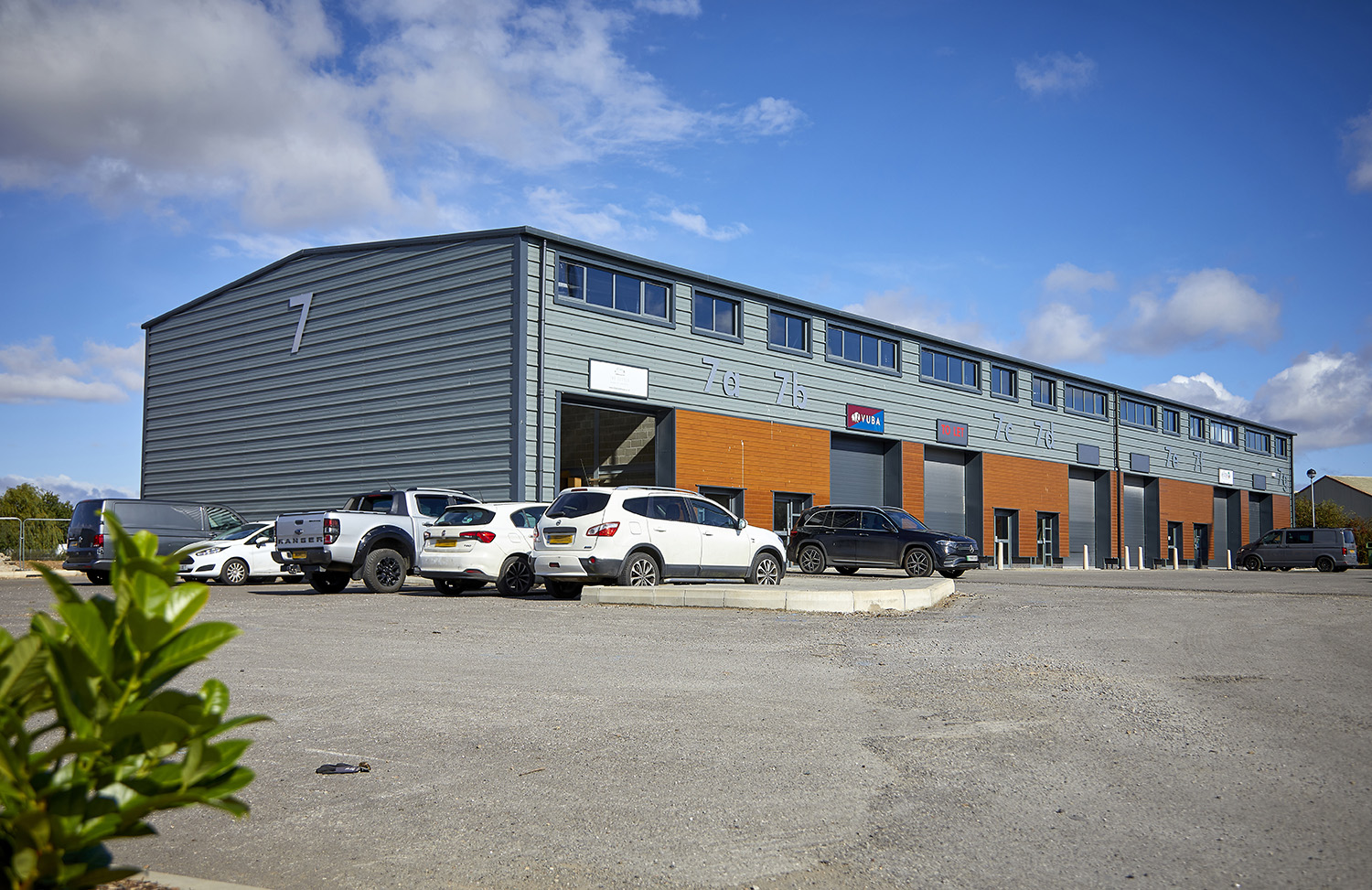 view from across a car park, of a grey steel and wood clad light industrial unit