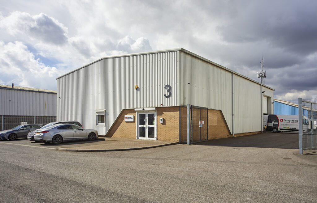 View from across a car park, of a white steel clad light industrial unit. 