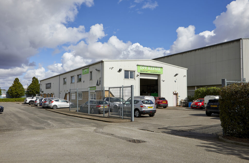 View from across a car park, of a white steel clad light industrial unit. Signage for DFF Repair on the building.