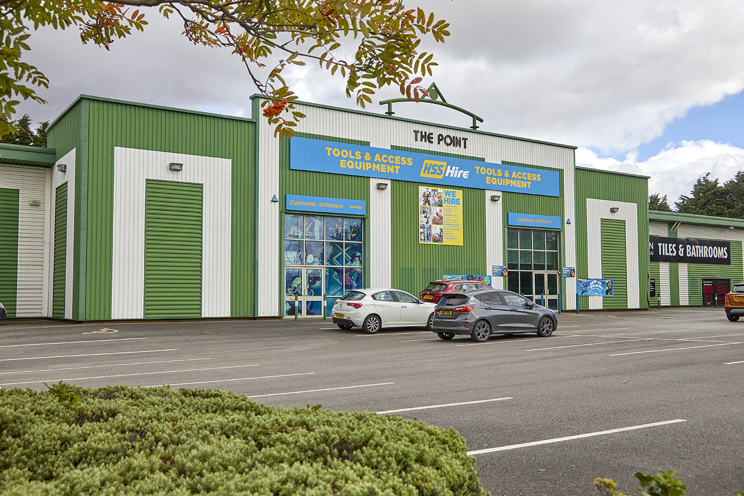 View from across a car park, of a green steel clad light industrial unit. Signage for HSS Tool Hire on the building.