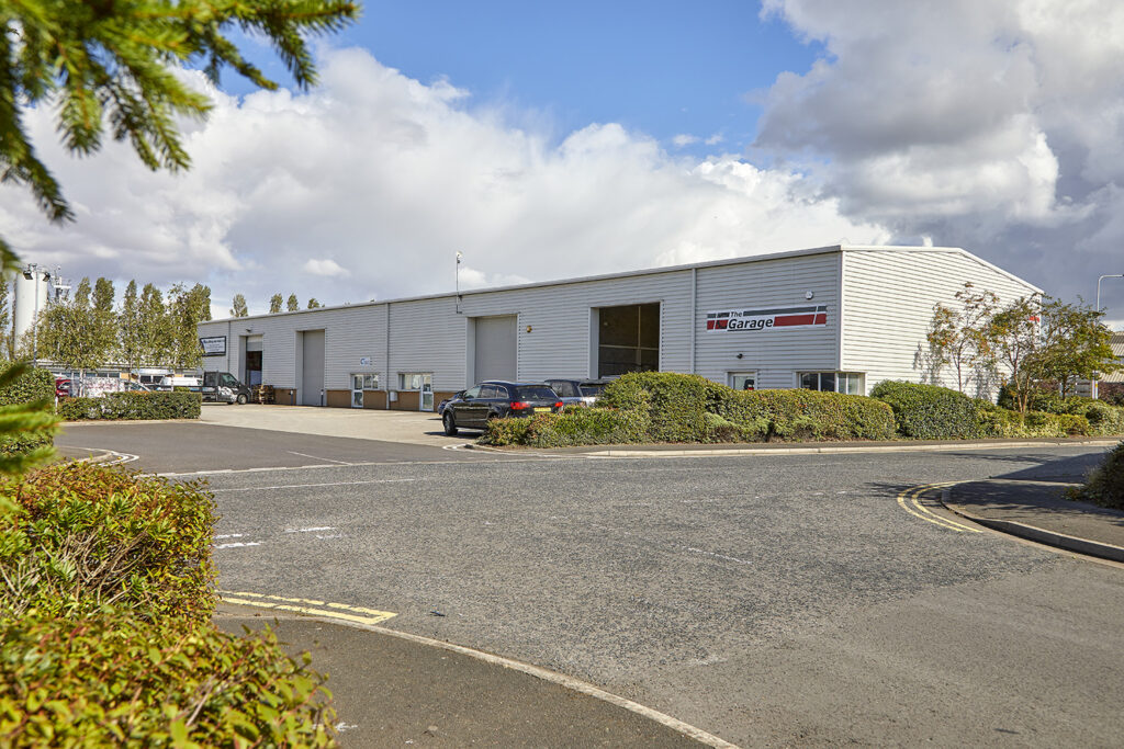 View from across a car park, of a white steel clad light industrial unit. Signage for The Garage Grimsby on the building.