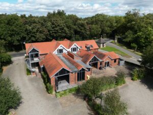 Drone view of an office building that s 2 storey, dormer style, brick-built. Trees to background and carpark to foreground of image