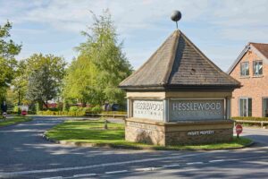 view down a driveway, with a 4-sided brick-built structure in the foreground. The structure has a pointed top and shows Hesslewood Office Park signage.