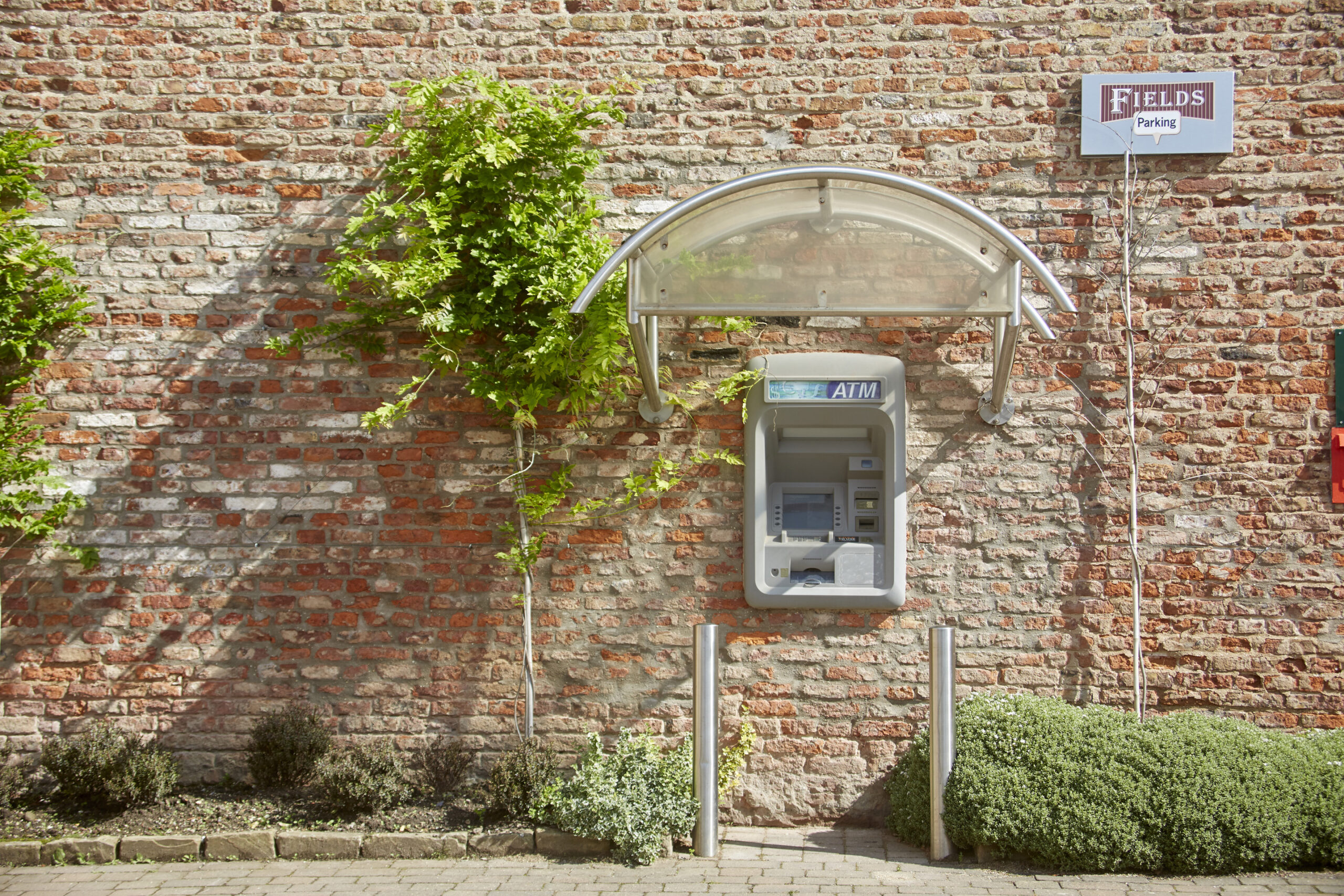 ATM machine, in a aged brick wall, with some shrubbery visible