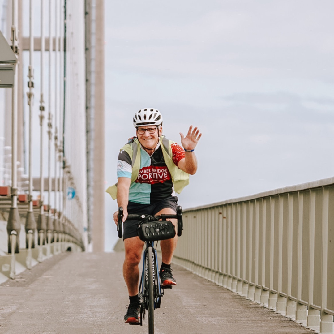 View of cyclist travelling on a bridge pathway, coming toward the camera and waving