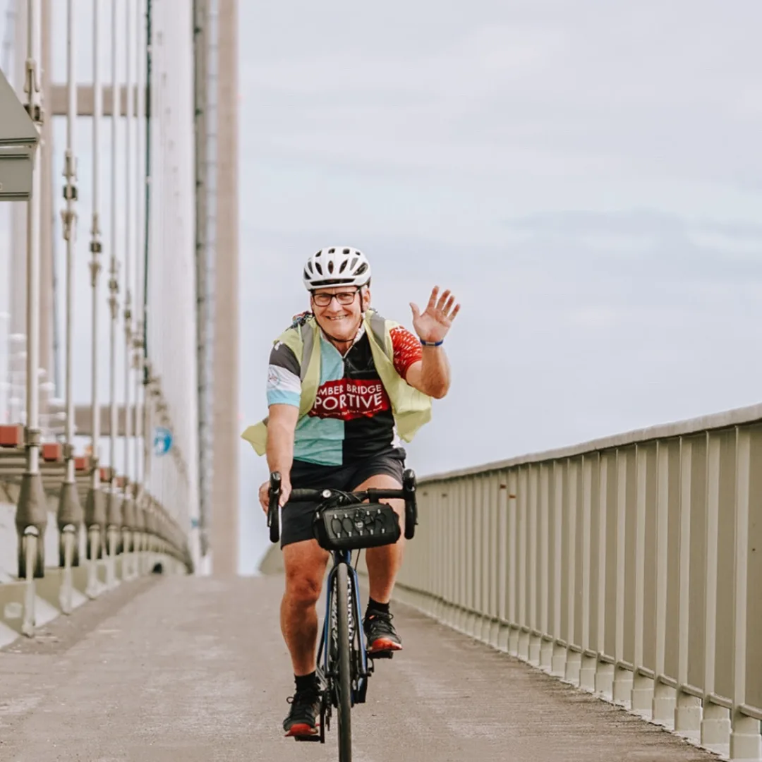 View of cyclist travelling on a bridge pathway, coming toward the camera and waving