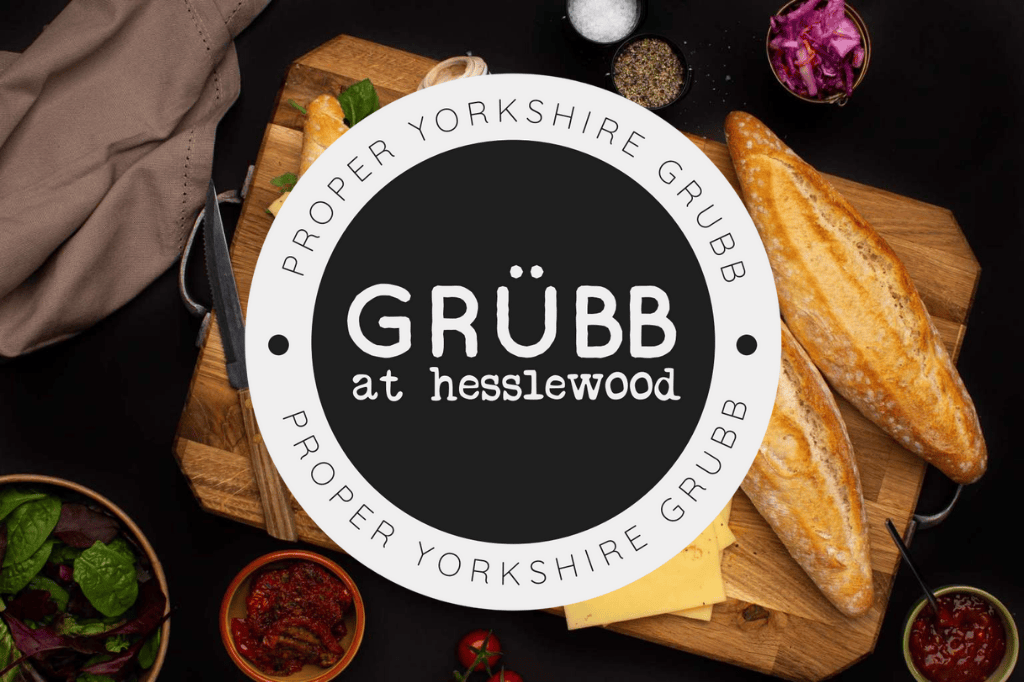 Background image of a panini sandwich on a wooden breadboard, over imposed with logo of 'Grubb at Hesslewood'