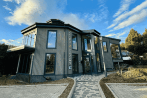 Modern two-story office building with large glass windows and a glass balcony, featuring the signage ‘Adams & Green’ on the exterior, located in a landscaped business park under a blue sky.