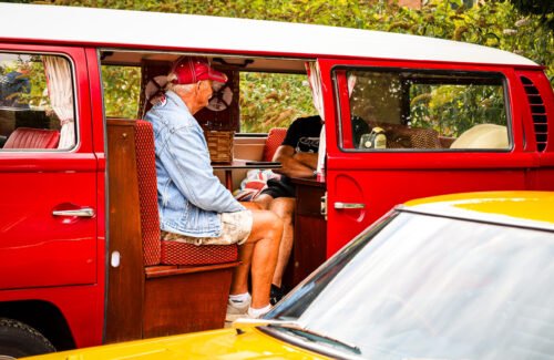 Classic Cars at Hesslewood 2026 Close up of male wearing cap, sat opposite another person, inside a red VW Campervan