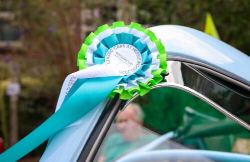 Classic Cars at Hesslewood 2026 Close up of a an award rosette in green, white and blue, that reads Classic Cars at Hesslewood 2026. attached to the bonnet of a pale blue vehicle.