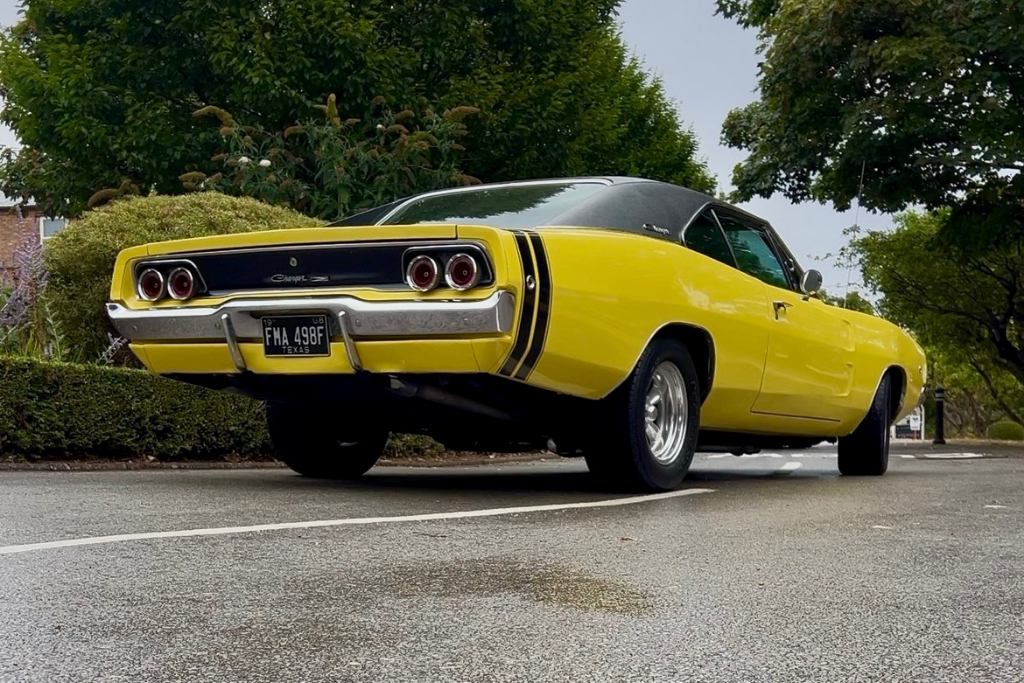 Low rise image, showing road with a rear view of a yellow classic vehicle pulling away