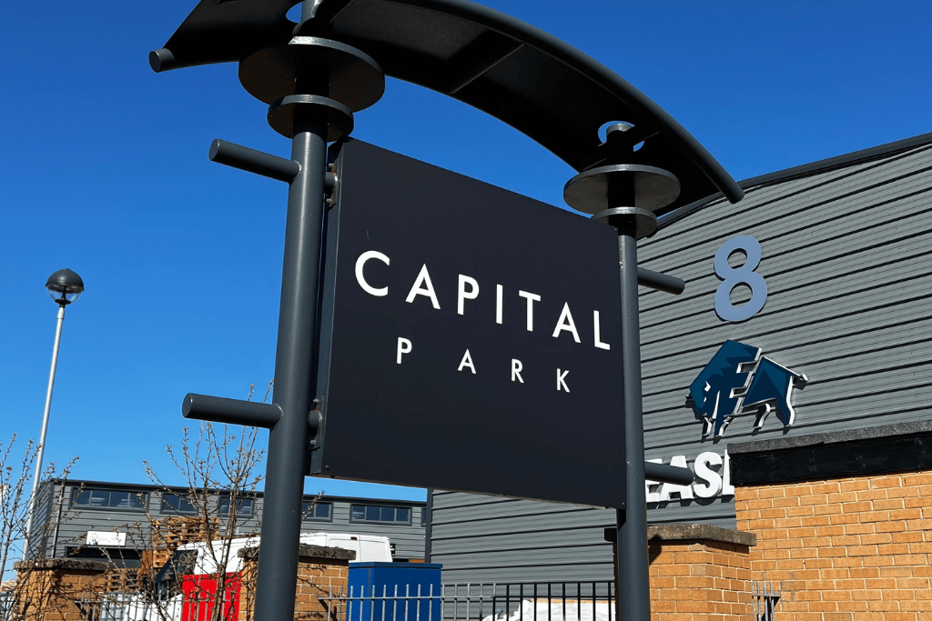 Forefront of the image is a large metal sign that reads 'Capital Park'. Behind are 2 modern idustrial units, the closest with a number 8 and Easihold branding on it.